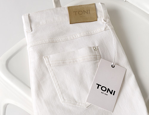 Zusammengelegte weiße TONI-Jeans mit Etikett auf weißem Stuhl – Teaser zur Retoure für Kundinnen aus Österreich