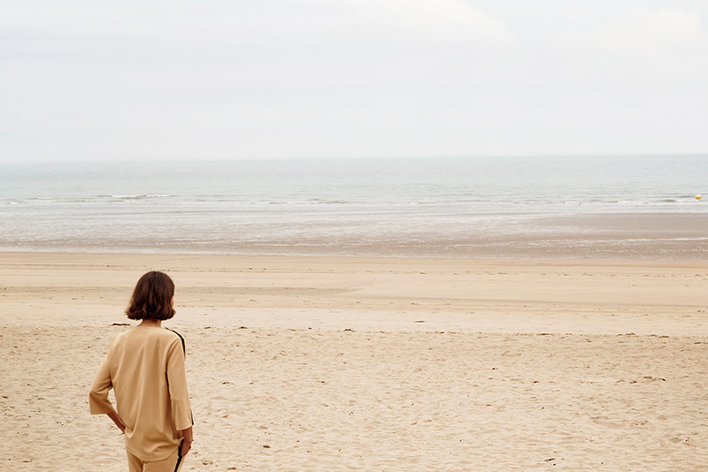 Delivered with Care – Our Shipping Promise. Woman looking out to sea from the beach – calm teaser for shipping & delivery at TONI.