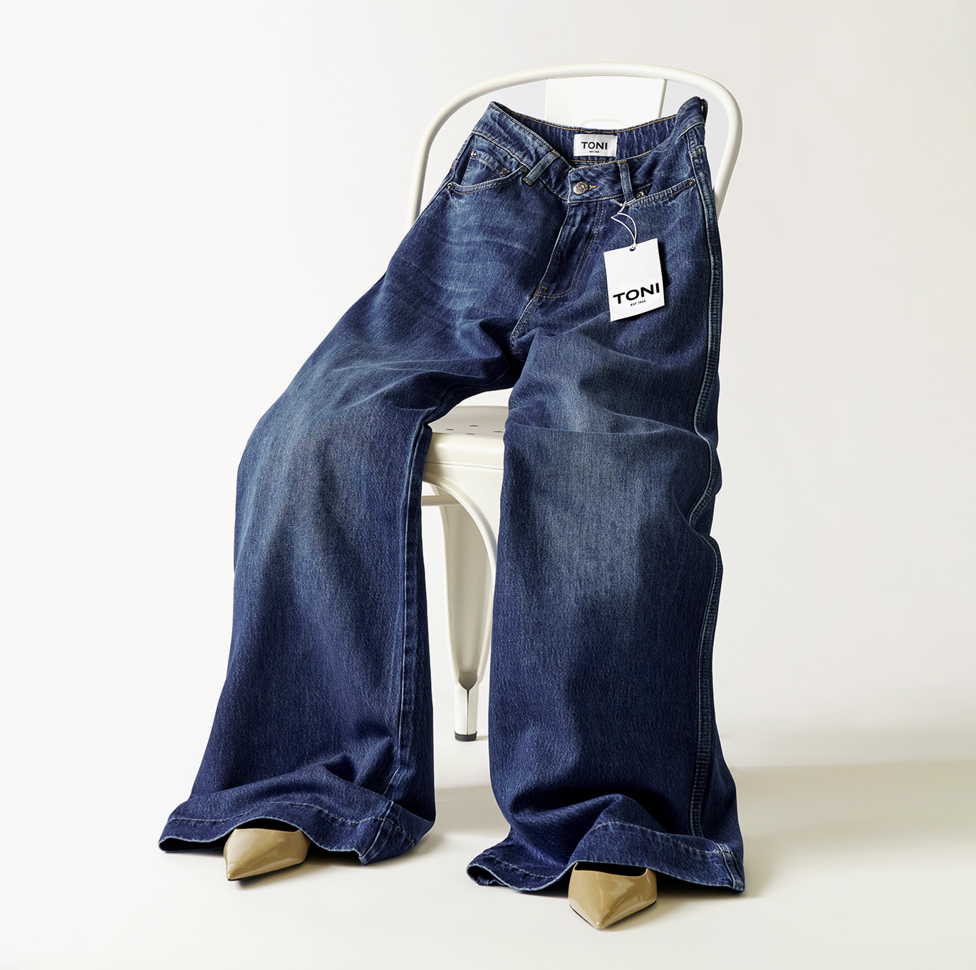 Dark blue wide-leg jeans with TONI label, casually styled on a chair – teaser for the jeans category in the online shop