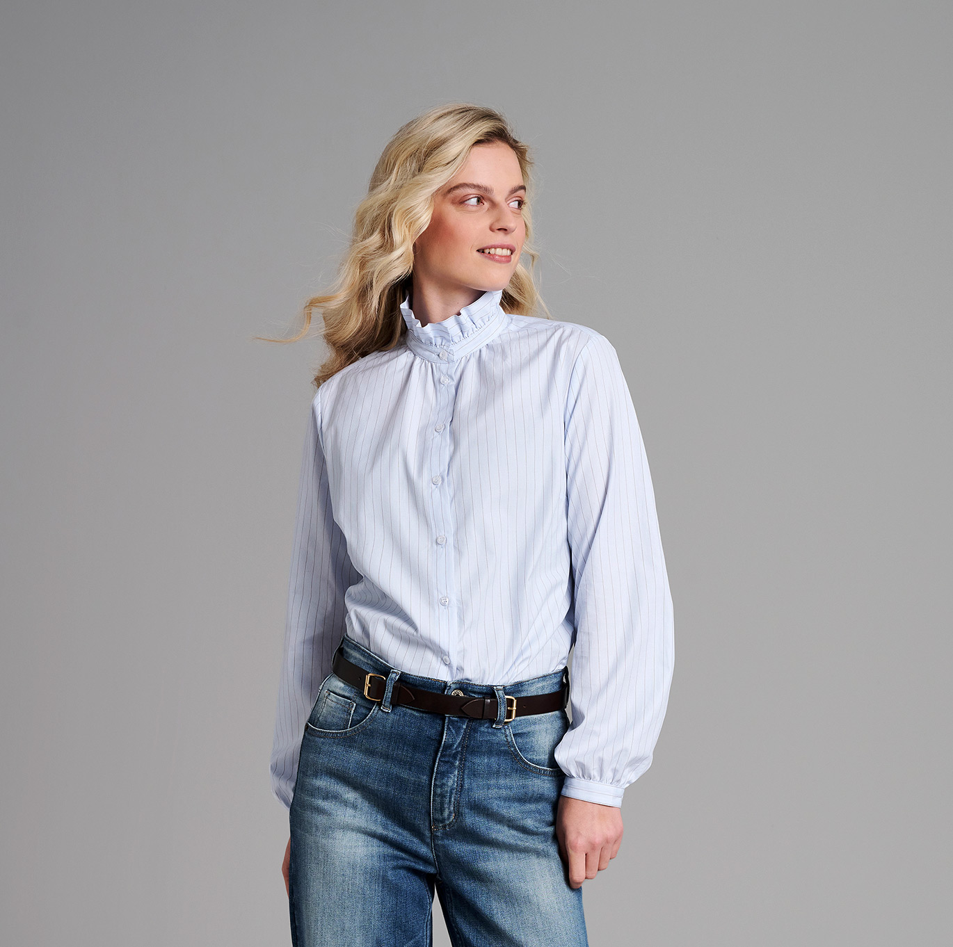 Frau in hellblauer gestreifter TONI-Bluse mit Rüschenkragen – Teaser zur Kategorie Oberteile.