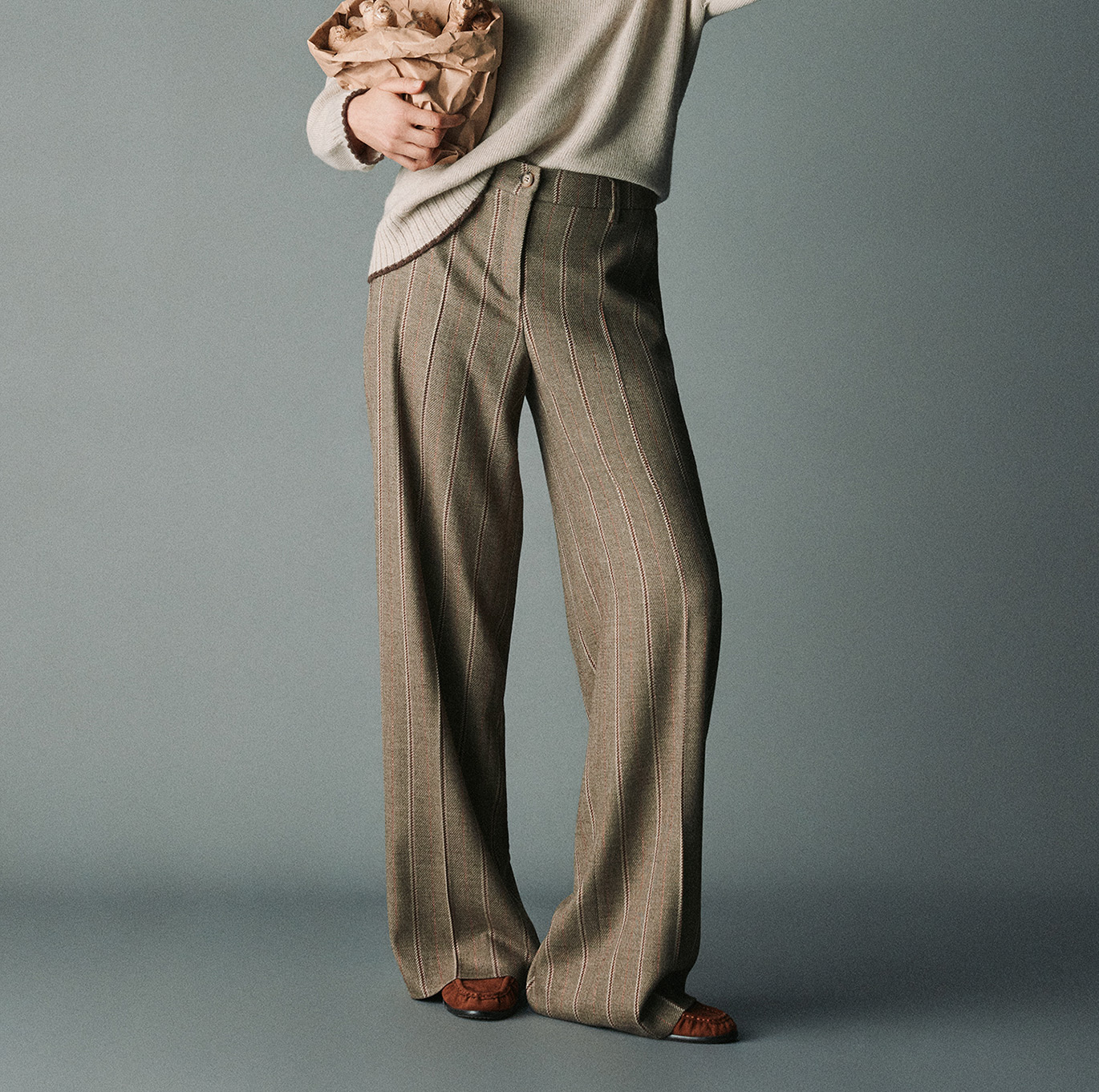 Model wearing wide-leg striped trousers by TONI with a light knitted sweater and brown loafers.