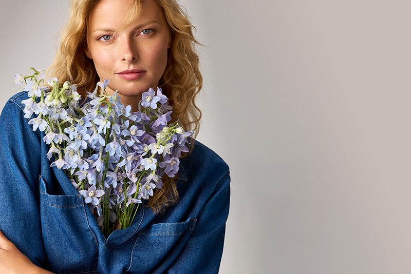 Modell in blauer Denim-Bluse mit Blumenstrauß – freundlicher Teaser zum Kundenservice von TONI